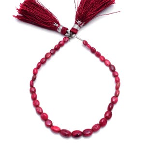 Pode incluir: Um fio de contas ovais de cor vermelho escuro com borlas em cada extremidade.