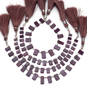 May include: Four strands of rectangular, deep magenta-colored gemstone beads arranged in a cascading arc. Each strand is finished with a long, brown silk tassel attached by a silver-toned metal cap and jump ring, with silver spacers between beads.