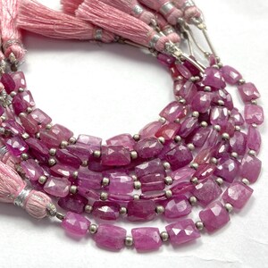 Puede incluir: Un collar de cuentas de piedras preciosas rosas, rectangulares y facetadas, intercaladas con pequeños espaciadores redondos de metal plateado. El collar termina con varias borlas de hilo rosa claro, aseguradas con tapas de metal plateado.