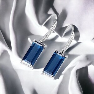 May include: A pair of silver dangle earrings with a rectangular blue gemstone and a clear crystal accent on the hook.