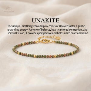 May include: A beaded bracelet featuring small, faceted, mottled green and pink Unakite stones interspersed with tiny gold-toned metal beads. It includes a gold-toned lobster clasp, an adjustable chain, and a small heart-shaped charm at the end.