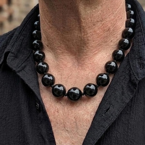 May include: A necklace composed of large, smooth, spherical black beads. The beads are uniform in size and strung together in a single strand that rests around the neck. The necklace features a high-gloss finish that reflects light on the surface.
