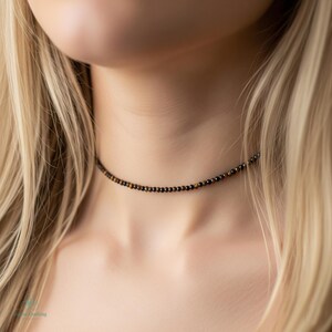 May include: A delicate choker necklace featuring small, round beads in shades of brown and black. The necklace is worn around the neck, showcasing the jewelry's subtle elegance. The beads appear to be evenly spaced, creating a minimalist design.