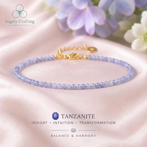 May include: A delicate bracelet featuring small, faceted, light purple tanzanite beads strung on a thin gold-toned chain. The bracelet includes a gold-toned lobster clasp and an adjustable extender chain with a small circular charm at the end.