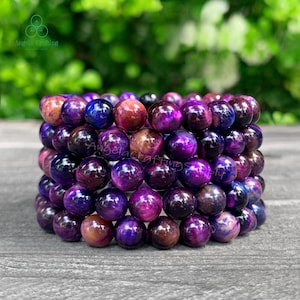 May include: A bracelet composed of multiple rows of polished, spherical beads in shades of deep purple, violet, and reddish-brown. The beads exhibit a chatoyant, silky luster with dark, swirling patterns throughout the smooth, rounded surfaces.