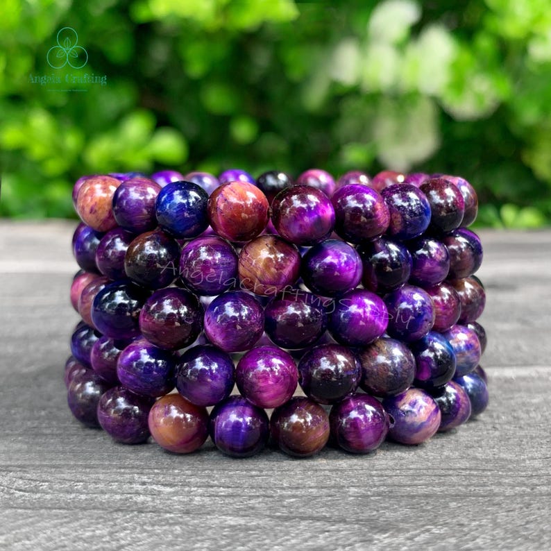 May include: A bracelet composed of multiple rows of polished, spherical beads in shades of deep purple, violet, and reddish-brown. The beads exhibit a chatoyant, silky luster with dark, swirling patterns throughout the smooth, rounded surfaces.