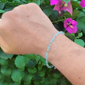 May include: A delicate bracelet featuring small, faceted light blue gemstone beads interspersed with tiny, polished silver-toned metallic spacer beads, arranged in a continuous circular strand that rests against the skin of a wrist.