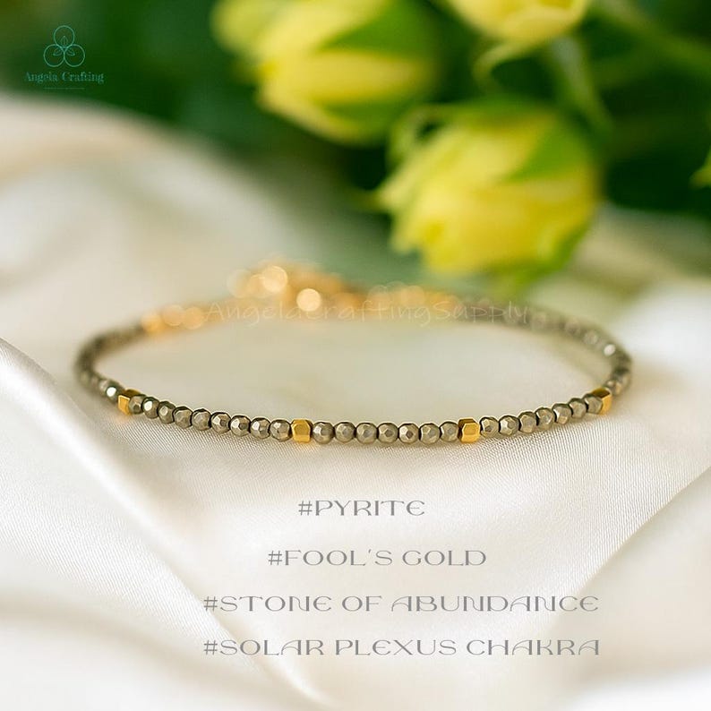 May include: A delicate bracelet featuring small, faceted metallic pyrite beads interspersed with smooth, polished gold-tone cube spacers. The jewellery piece includes a thin chain extension and is presented with the text #PYRITE #FOOL'S GOLD #STONE OF ABUNDANCE #SOLAR PLEXUS CHAKRA.