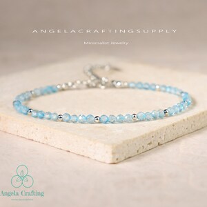 May include: A delicate bracelet featuring small, faceted light blue beads interspersed with polished silver-tone metal spheres. The piece includes a silver-tone metal chain extension and clasp. Text reads ANGELACRAFTINGSUPPLY and Minimalist Jewelry.