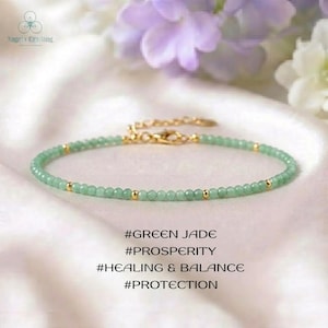 May include: A delicate bracelet featuring small, round, light green jade beads interspersed with tiny gold-toned metal beads. The piece includes a gold-toned lobster clasp and chain extender. Text reads: #GREEN JADE #PROSPERITY #HEALING & BALANCE #PROTECTION.
