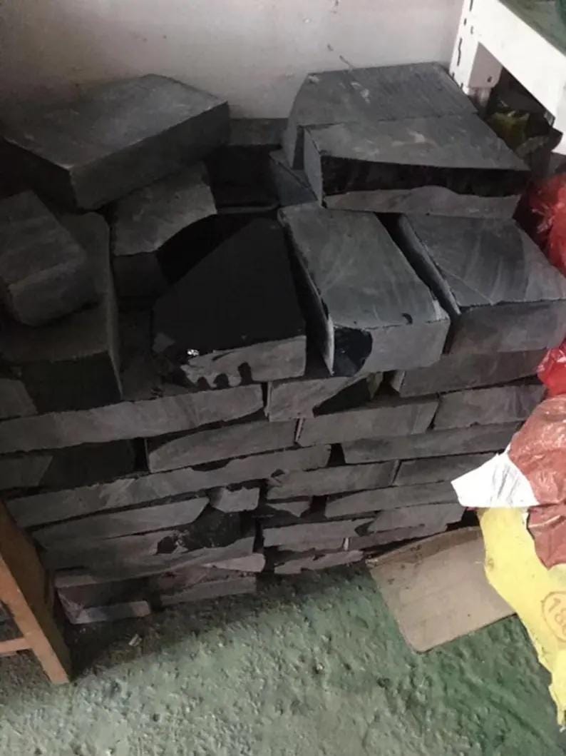 May include: A stack of rectangular dark gray stone blocks with rough, textured surfaces. The stones are arranged in multiple layers, showing varying thicknesses and irregular edges. Some blocks feature smooth, dark, reflective patches on their tops.
