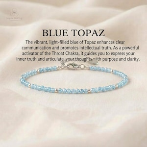 May include: A delicate bracelet featuring small, faceted light blue topaz beads interspersed with tiny silver-toned metal spheres. The piece includes a silver-toned lobster claw clasp and a small heart-shaped charm. Text reads: BLUE TOPAZ.