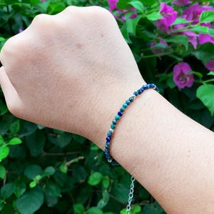 May include: A delicate bracelet made with small, round beads in shades of blue and green. The beads are strung on a silver chain.