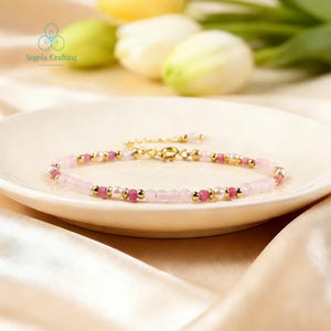 May include: A delicate beaded bracelet featuring alternating light pink rose quartz beads, small white pearls, vibrant fuchsia gemstone beads, and polished gold-tone metal spacers. The bracelet includes a gold-tone lobster claw clasp closure.