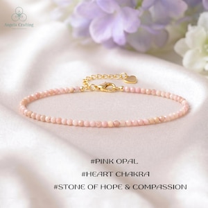 Pode incluir: Uma pulseira delicada com pequenas contas de opala rosa facetadas em uma corrente fina de tom dourado. A pulseira inclui um fecho lagosta dourado e um pequeno pingente em forma de coração. O texto na imagem diz #PINK OPAL #HEART CHAKRA #STONE OF HOPE & COMPASSION.