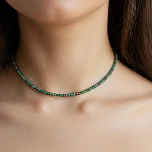 Puede incluir: Un delicado collar choker de piedras preciosas verdes y rosas. El collar está hecho de pequeñas cuentas facetadas que están enhebradas en una cadena fina.