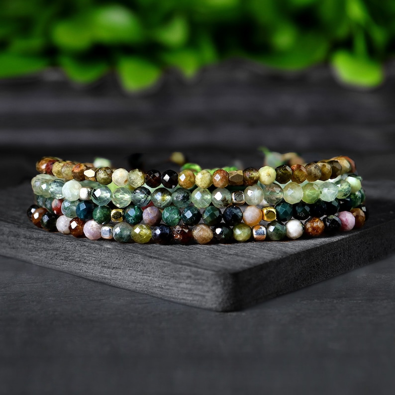 May include: A set of five bracelets made with various green, brown, and black gemstone beads. The bracelets are stacked on top of each other and are tied together with a thin string.