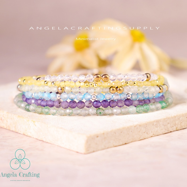May include: A stack of five beaded bracelets featuring faceted clear, yellow, light blue, purple, and green beads interspersed with small metallic gold and silver spheres. The text ANGELACRAFTINGSUPPLY and Angela Crafting are visible.