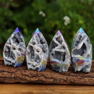May include: Four iridescent quartz crystal geodes with a teardrop shape. The crystals have a gray and white interior with a rainbow sheen at the top and bottom. They are displayed on a piece of brown wood.