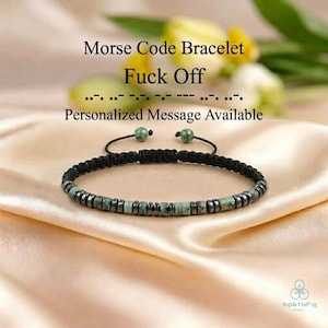 May include: A Morse code bracelet featuring alternating turquoise-colored stone discs and dark metallic beads on a black cord. The text "Morse Code Bracelet Fuck Off" and "Personalized Message Available" is printed above the bracelet.