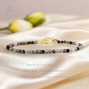 May include: A delicate bracelet composed of small, faceted black and white tourmaline beads with a gold-toned metal clasp. The text #ROOT CHAKRA, #BLACK TOURMALINE, and #GROUNDING PROTECTION is visible below the jewelry piece.