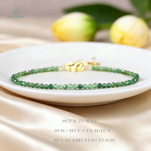 May include: A delicate bracelet composed of small, faceted green gemstone beads arranged in a circular pattern. The piece features a gold-toned metal clasp mechanism at the center, providing a secure closure for the thin, circular strand of beads.