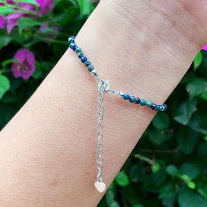 May include: A blue and green gemstone bracelet with a silver chain and heart charm.