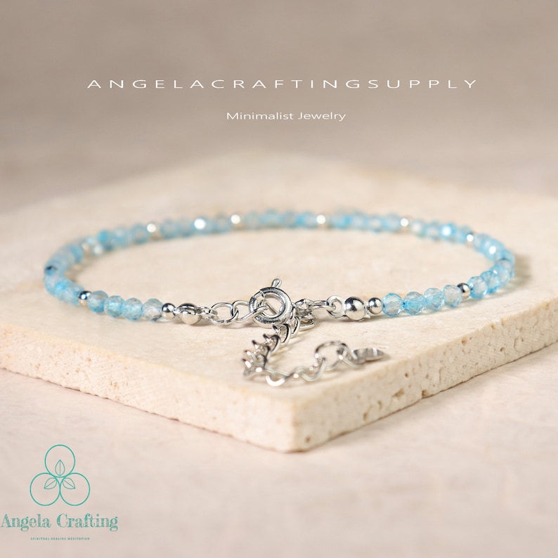 May include: A delicate bracelet featuring small, faceted light blue beads interspersed with tiny silver-toned metal spheres. The piece includes a silver-toned spring ring clasp and an adjustable chain extension with a small circular metal tag.