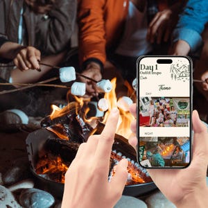 May include: A smartphone displaying a mobile app with the text "Day 1 Outfit Inspo" and a theme selection for day and night. The phone is being held by a hand in front of a campfire with people toasting marshmallows.