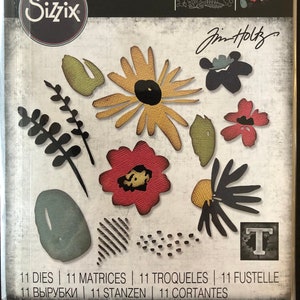 May include: A set of 11 die-cut metal stencils for crafting. The stencils feature floral designs in shades of red, yellow, green, and black. The package includes the text "THINLITS®" and "Jim Holtz".