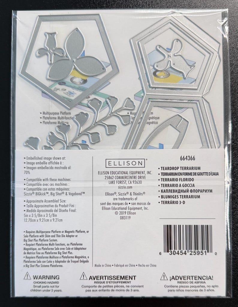 Puede incluir: Un juego de troqueles de metal Sizzix Thinlits para un terrario en forma de gota, modelo 664366. El paquete incluye troqueles plateados con formas de marcos geom&eacute;tricos y flores. La etiqueta muestra el nombre del producto y datos.