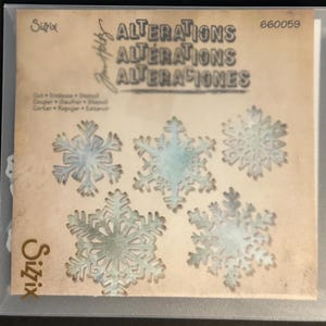 May include: A package of Sizzix Alterations stencils featuring five snowflake designs. The stencils are in various sizes and have a distressed, vintage look. The package includes the text "Alterations" and "660059".