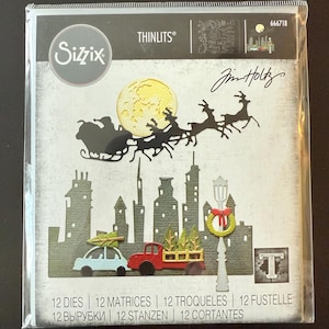May include: Sizzix Thinlits die set featuring a Christmas theme. The design includes a silhouette of Santa's sleigh with reindeer, a cityscape, and festive vehicles. The package includes 12 dies, 12 matrices, and 12 other components.