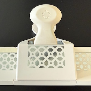 May include: A white Martha Stewart paper punch with a geometric design. The punch has a large handle and a decorative pattern on the front and sides. The Martha Stewart logo is visible on the handle.