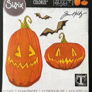 May include: A Sizzix Thinlits Colorize die set by Tim Holtz, model 665556, featuring 12 metal cutting dies. The packaging displays die-cut images of two orange jack-o'-lantern pumpkins with green stems and two brown bats on a white background.