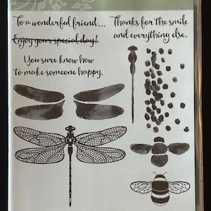 May include: Clear plastic packaging containing a set of rubber stamps with dragonfly and bee designs. The set includes stamps of dragonfly wings, a dragonfly, a bee, and other nature-themed images. Text includes "Dragonfly Dreams" and inspirational phrases.