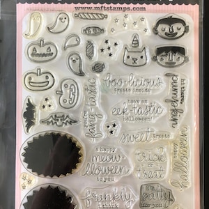 May include: Clear stamp set featuring Halloween-themed designs. Includes images of ghosts, pumpkins, a cat with a unicorn horn, and various phrases like "boo-licious" and "sweet treats." The set is packaged in a clear plastic sleeve.