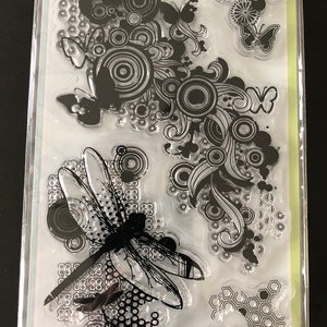 May include: A set of five clear stamps featuring a dragonfly, a bee, a ladybug, and two butterflies. The stamps are on a white background with the text "5 clear stamps" and "Inkadinkado" printed on the top.