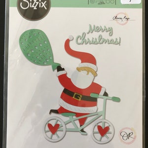 May include: A green and white die cut of Santa Claus riding a bicycle with a red heart on each wheel. He is holding a green and white balloon that says "Merry Christmas!" in a white script font. The die cut is part of a Sizzix Thinlits die set.