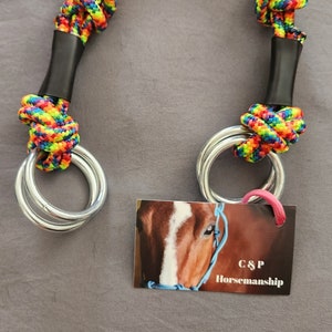 May include: A rainbow colored rope halter with two silver rings. The halter is made of two strands of rope that are tied together with a knot. The halter is labeled with the text "C&P Horsemanship".