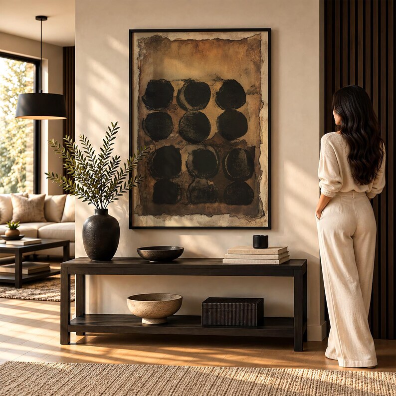 May include: A rectangular black wooden console table with two tiers, featuring a black vase with green foliage, a dark bowl, a stack of books, and a black box. Above the table hangs a large framed abstract painting with black circles.
