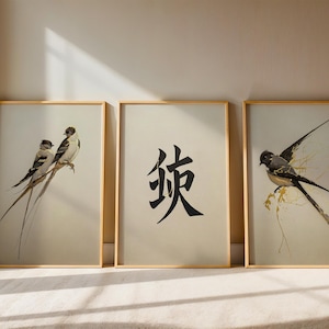 Könnte beinhalten: Drei gerahmte Kunstdrucke mit goldenen Rahmen. Die Drucke zeigen Aquarellillustrationen von Vögeln und ein schwarzes Kalligraphiezeichen auf cremefarbenem Hintergrund. Die Vögel haben lange Schwanzfedern und sitzen auf Ästen.