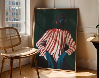 Puede incluir: Una impresión artística enmarcada que presenta una figura con una camisa a rayas rojas y blancas y pantalones azules. La obra de arte está ambientada sobre un fondo verde oscuro. La impresión se exhibe en una habitación con una silla de madera y una ventana.