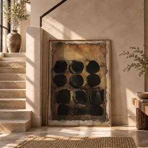 May include: A rectangular wall art piece in a thin gold frame featuring a grid of nine solid black circles set against a textured, layered background of deep brown, tan, and cream tones, creating a high-contrast abstract composition.