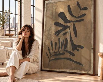 May include: A large rectangular framed wall art piece featuring a dark brown abstract botanical leaf silhouette centered on a textured tan background. The artwork is enclosed in a thin dark wood frame with a visible border.