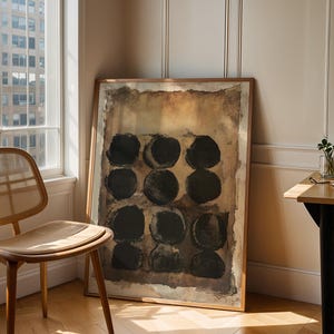 May include: A rectangular framed wall art piece featuring a grid of twelve solid black circles arranged in four rows of three. The background of the artwork consists of layered, textured shades of brown, tan, and beige with a distressed, weathered appearance.
