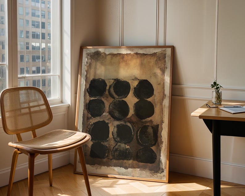 May include: A rectangular framed wall art piece featuring a grid of twelve solid black circles arranged in four rows of three. The background of the artwork consists of layered, textured shades of brown, tan, and beige with a distressed, weathered appearance.