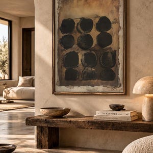 May include: A framed rectangular wall art piece featuring nine dark black circular shapes arranged in a grid pattern against a textured, mottled brown and tan background, enclosed within a thin, metallic bronze-toned frame.