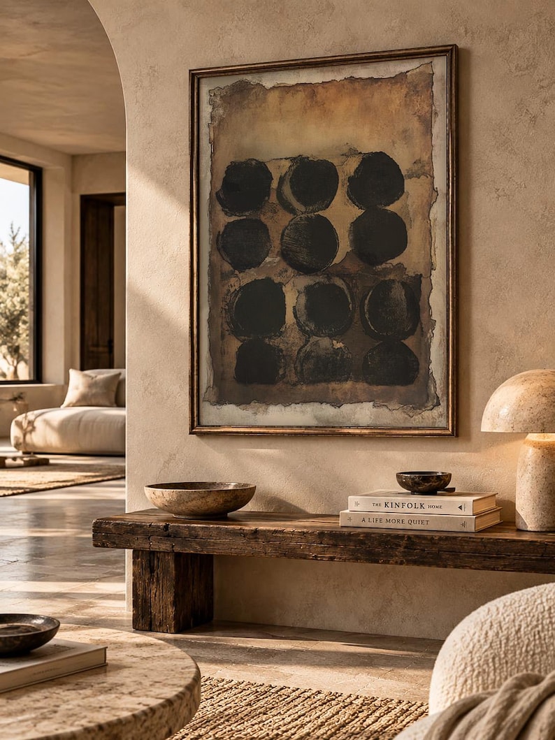 May include: A framed rectangular wall art piece featuring nine dark black circular shapes arranged in a grid pattern against a textured, mottled brown and tan background, enclosed within a thin, metallic bronze-toned frame.