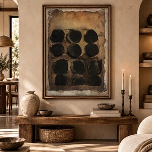 May include: A rectangular framed wall art piece featuring a grid of nine dark black circles set against a textured, layered background of muted brown, tan, and cream tones. The artwork is enclosed in a thin, dark metallic frame with a weathered finish.